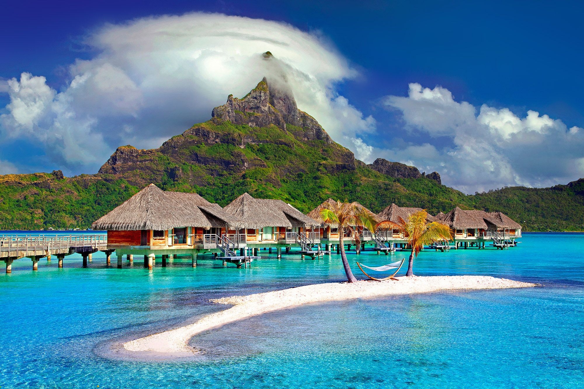Bungalow sull’acqua in Polinesia, mare turchese, motu con palme e hammock, scenario tropicale ideale per un viaggio da sogno.
